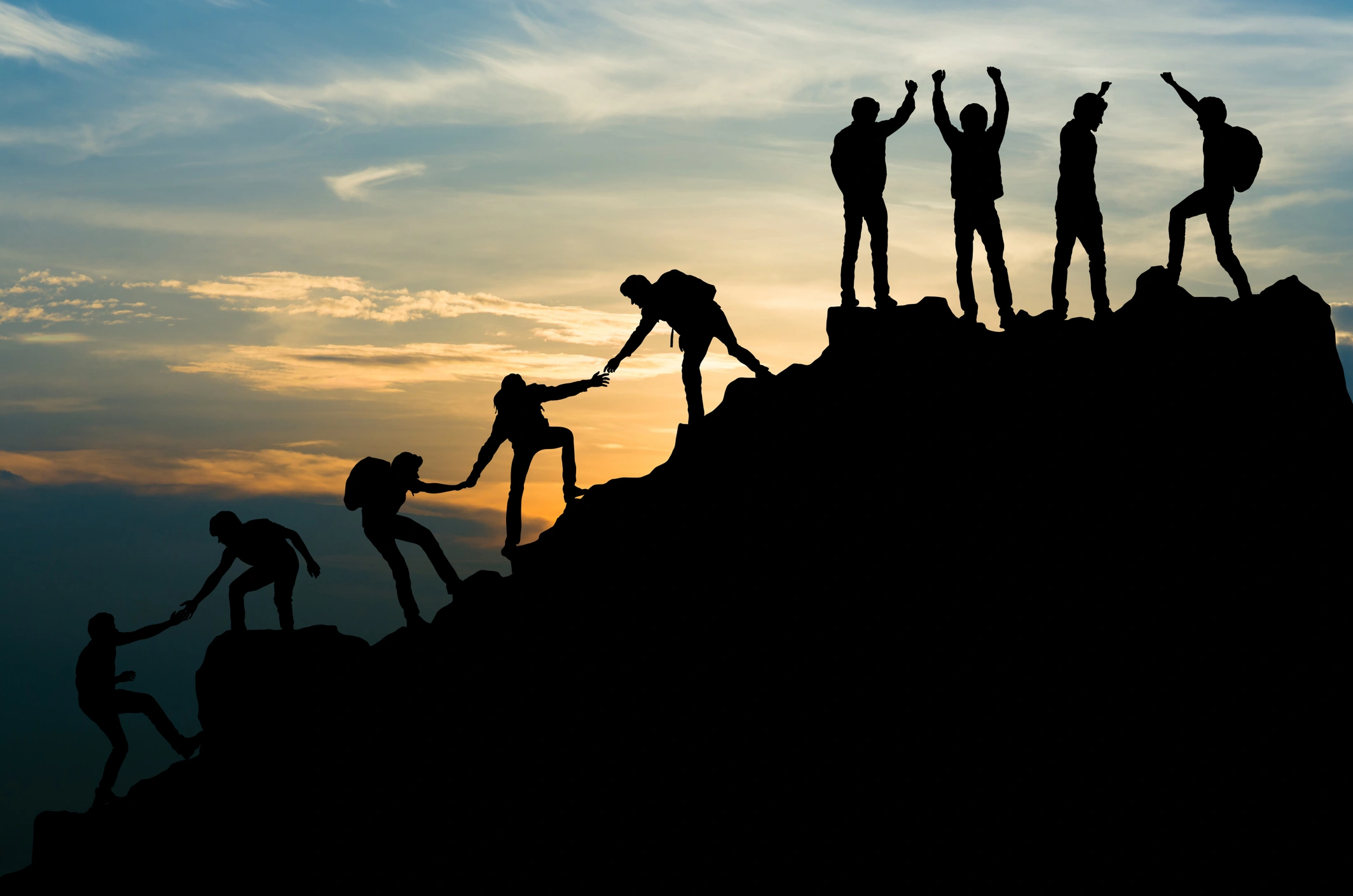 Group of people climbing up a mountain at sunset, with the sky in the background filled with clouds