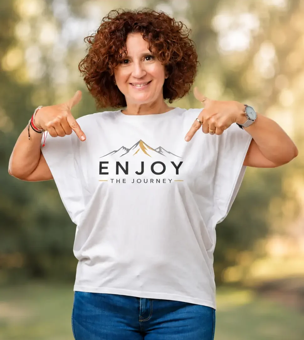 Woman standing and wearing a t-shirt with the words "enjoy the journey" printed on it, against a blurred background