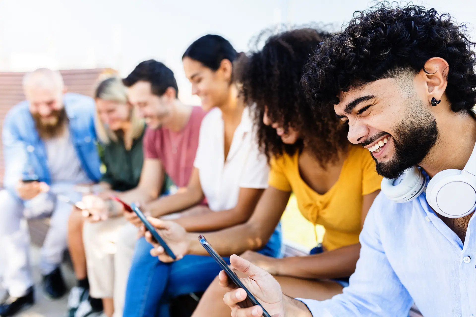 Group of people sitting on a bench, each of them holding a mobile phone in their hands and wearing headphones